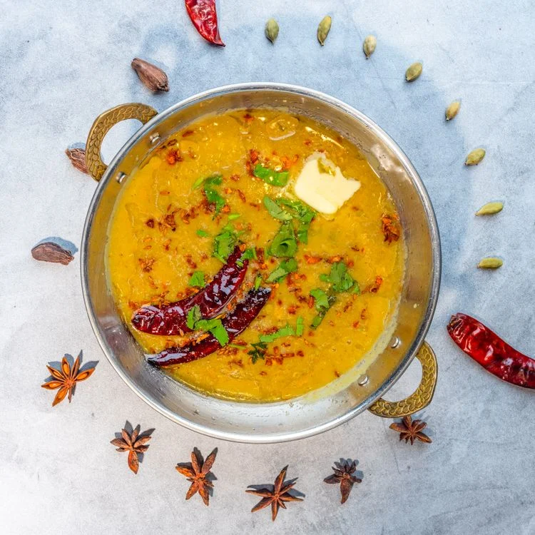 Indian dal tadka served in a traditional brass bowl, garnished with spices — eating this before rice significantly reduces blood sugar spikes