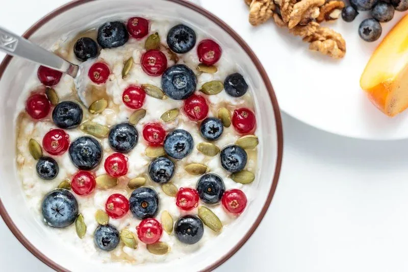 Bowl of plain Greek yogurt topped with fresh pomegranate seeds and honey
