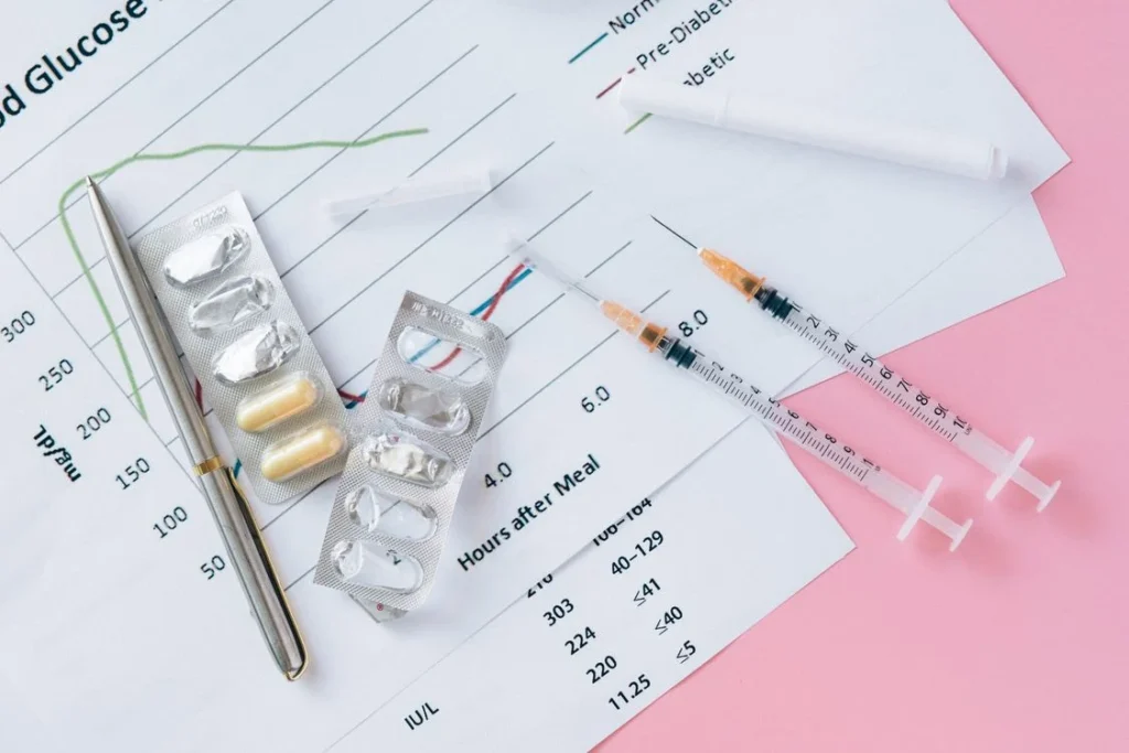 Flat lay of diabetes medicines, syringes and blood sugar chart on a pink background