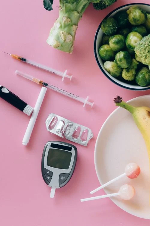 Glucometer next to fruits and vegetables on a pink background representing diabetes-friendly foods