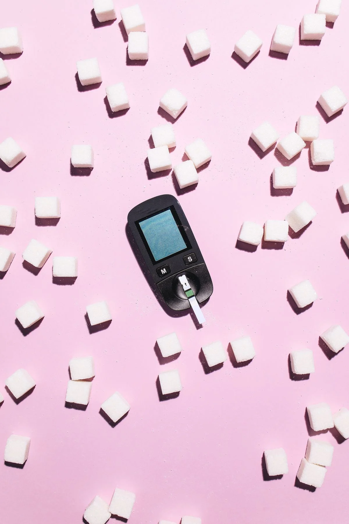 Glucometer with sugar cubes illustrating the link between sugar and blood glucose
