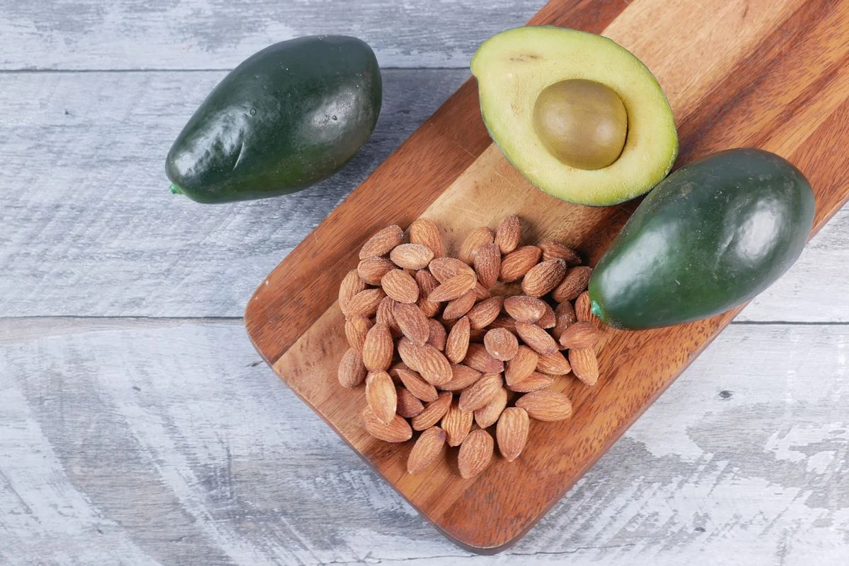 Almonds and avocado halves on a wooden board — whole food staples for a diabetes-friendly shopping list