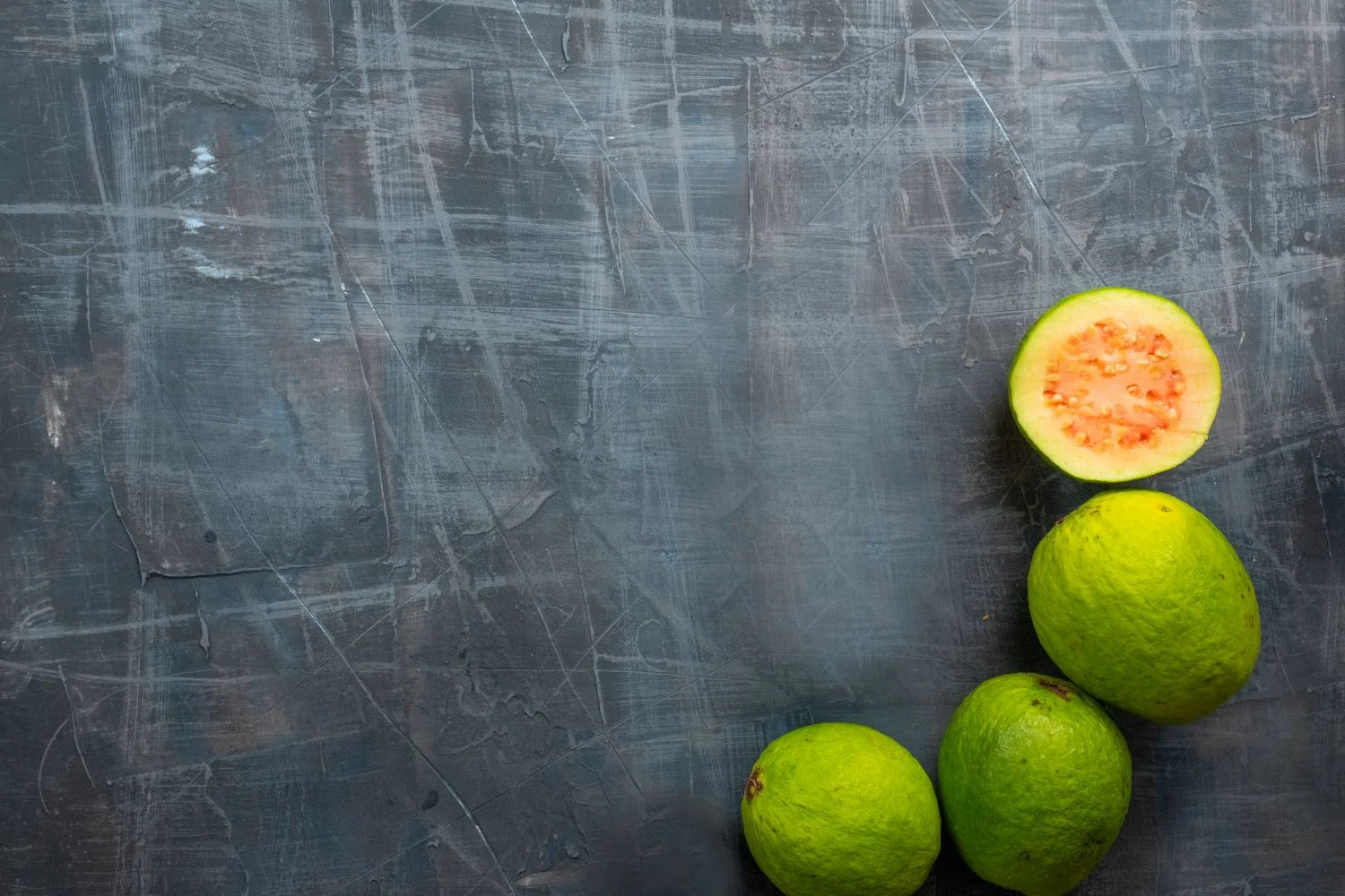 Top view of fresh guavas arranged on a surface — whole and halved to show pink flesh